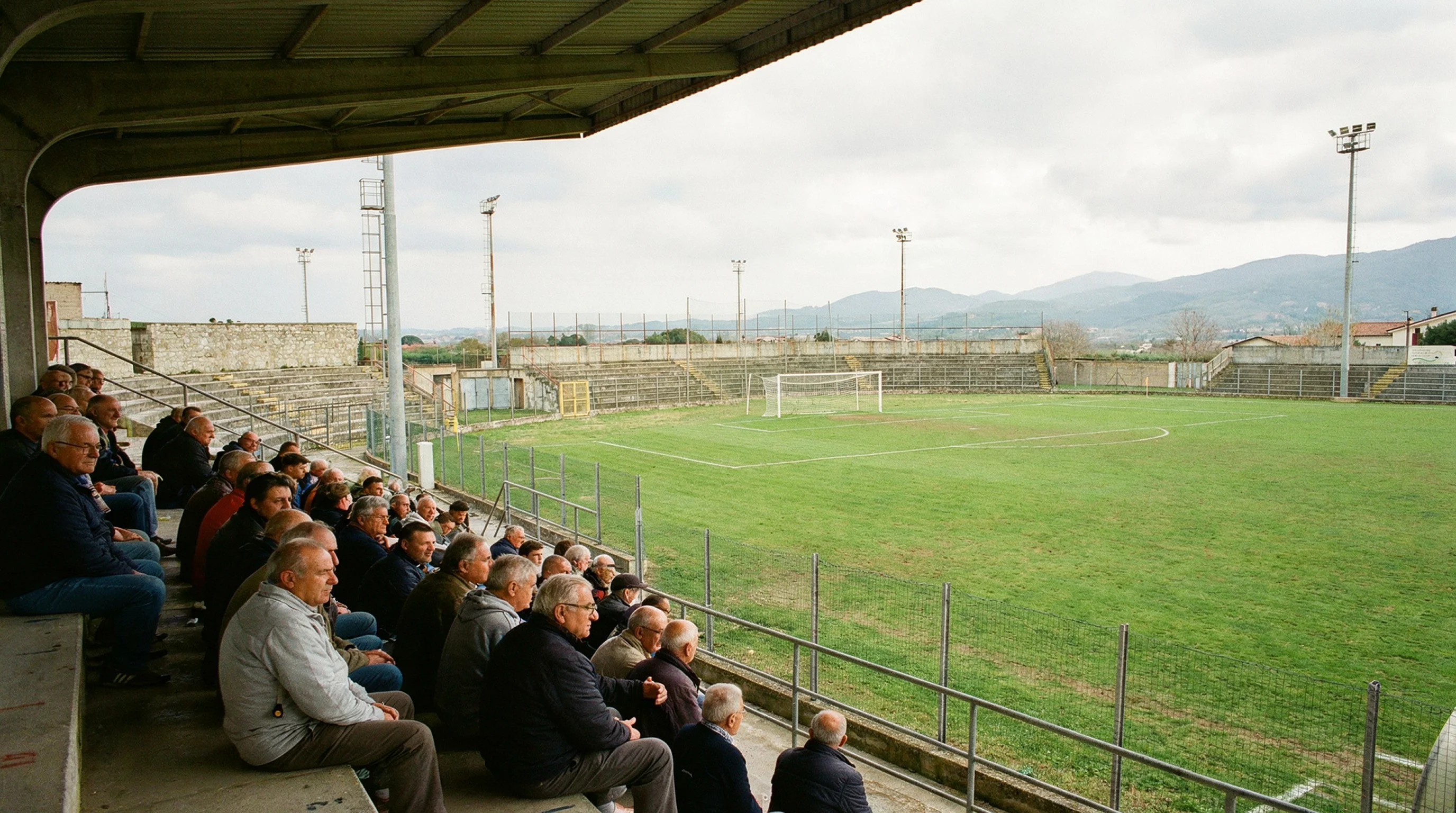 Piccolo stadio di calcio italiano di provincia con tribune e campo verde